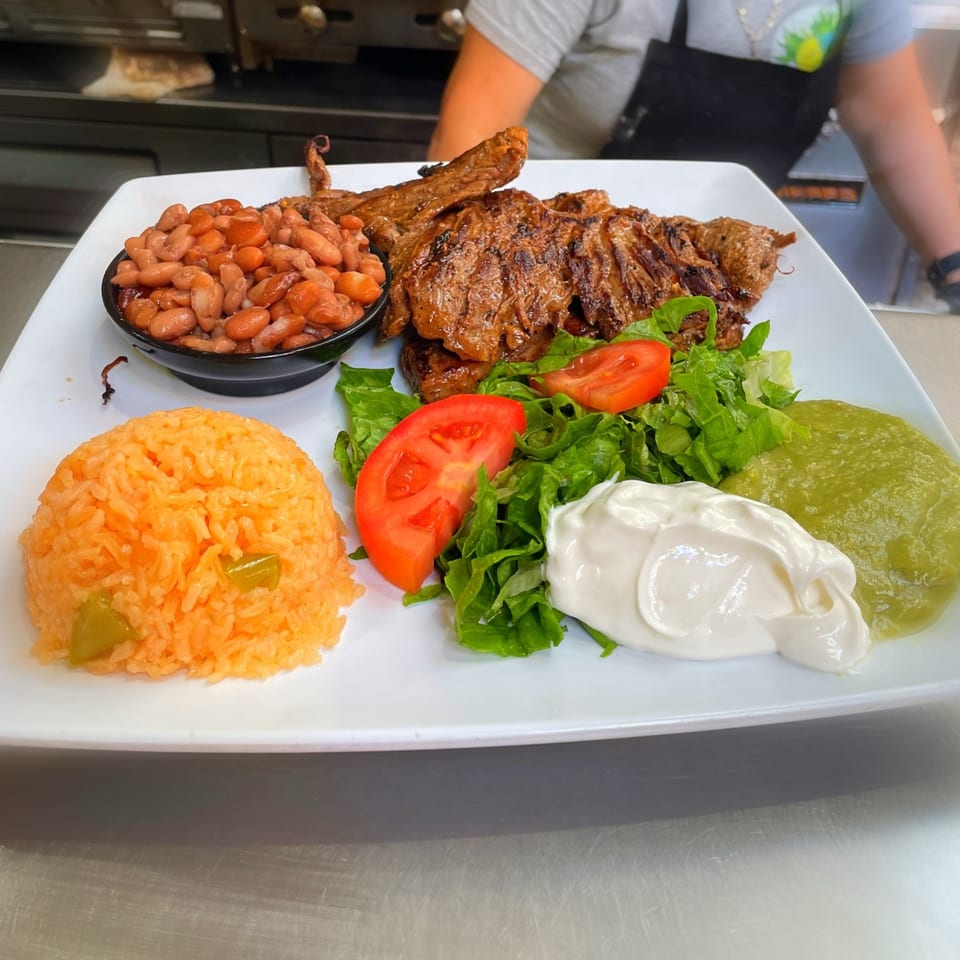 Grilled steak with rice, beans, salad, guacamole, and sour cream on a white plate.