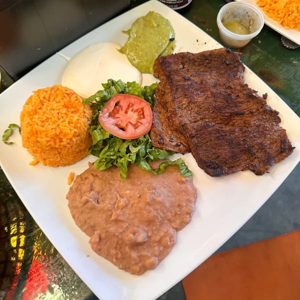 A Calafia Taqueria plate with carne asada, rice, refried beans, lettuce, tomato, guacamole, and sour cream.