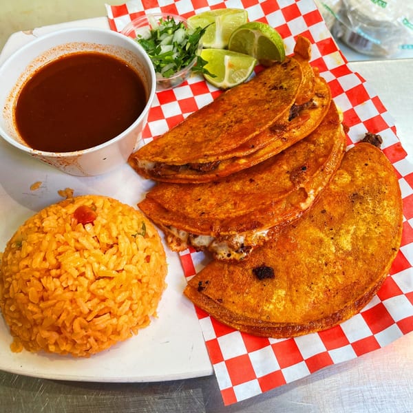 Three cheesy birria tacos with a side of red rice, consommé, limes, and chopped onions.
